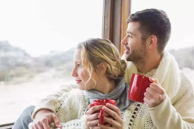 Happy couple with mugs looking out the window at one of our 1 bedroom Gatlinburg cabin rentals.